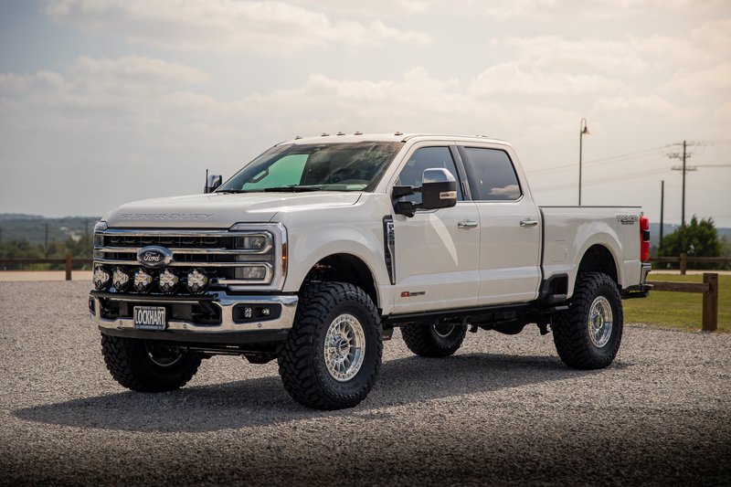White Ford F-250 Super Duty with aftermarket rims and off-road tires.