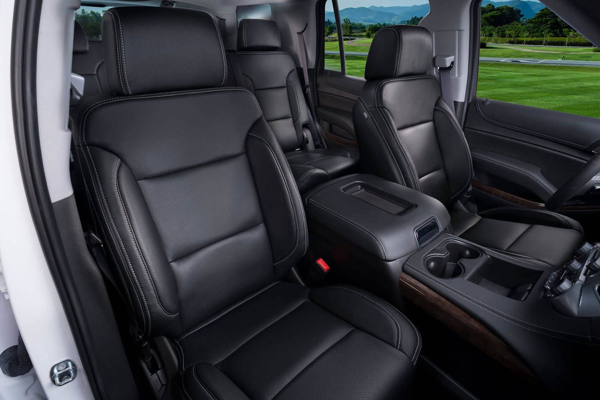 Black perforated leather front seats, center console with cupholders and wood trim in a Chevrolet Tahoe/Suburban SUV cabin