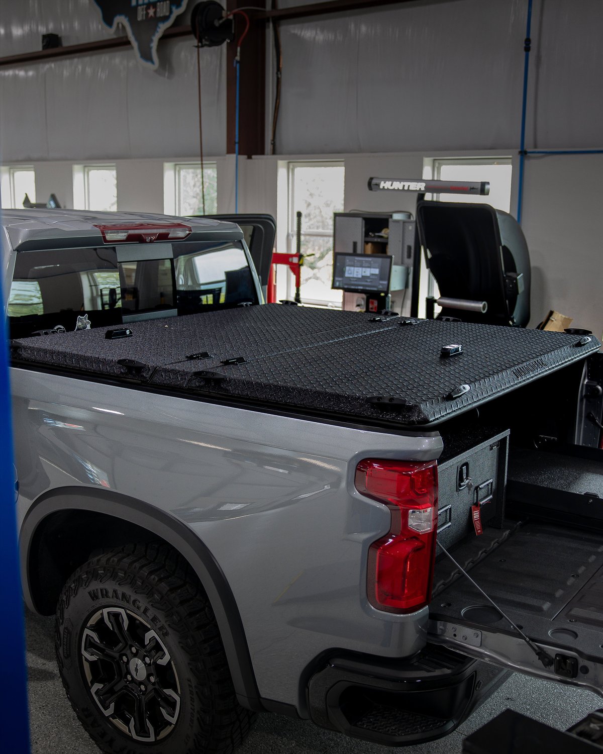 Gray pickup truck with a diamond-plate bed cover, Wrangler tires, and black trim.