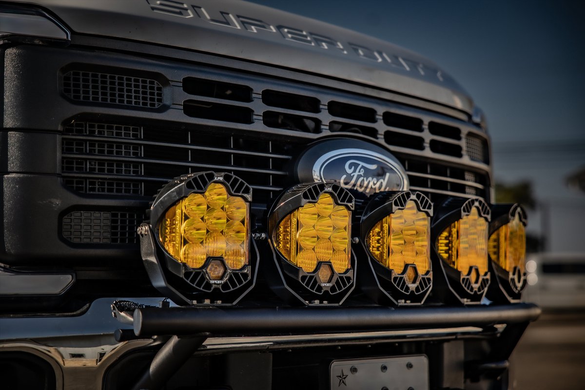 Black Ford Super Duty truck with multiple amber auxiliary lights mounted on a brush guard.