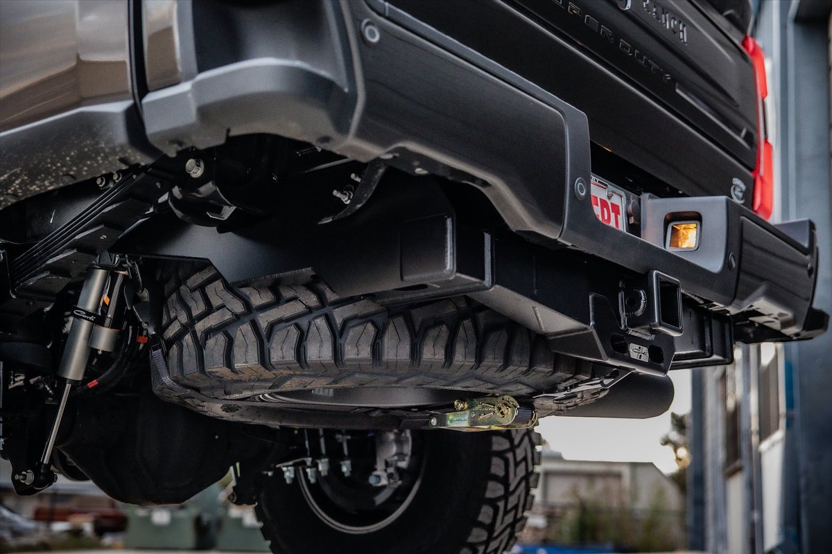 Black Ford Super Duty truck rear bumper, spare tire, and hitch receiver.
