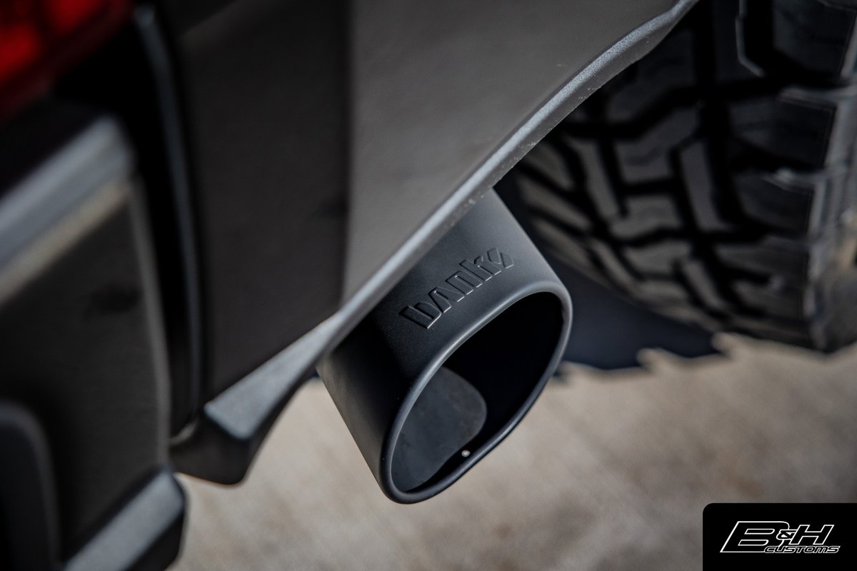 Close-up of a Ford F-350's black Banks exhaust tip with tire tread visible.
