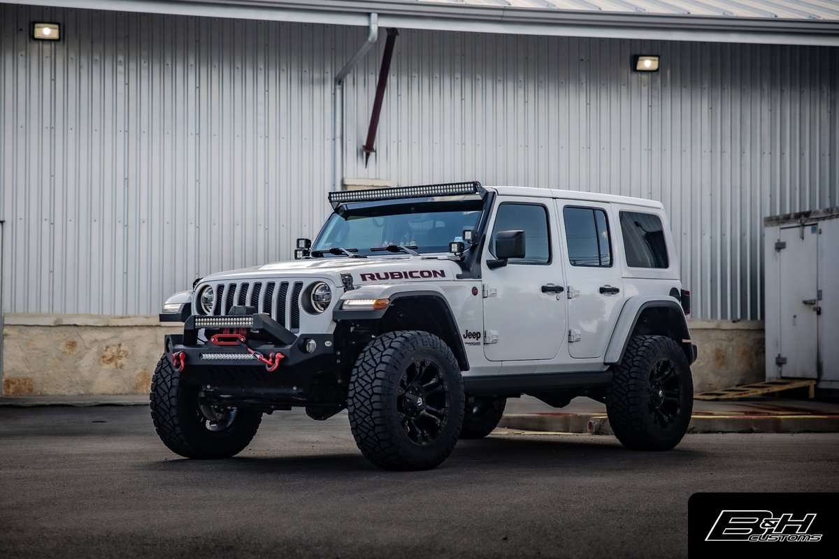 White Jeep Wrangler Rubicon with custom black rims, off-road tires, and light bar.