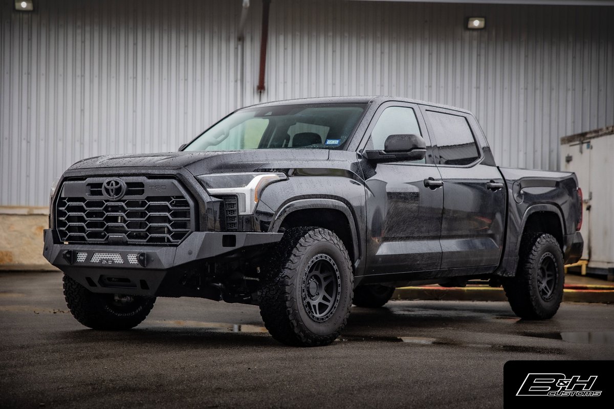 Black Toyota Tundra with aftermarket bumper, rims, and all-terrain tires.